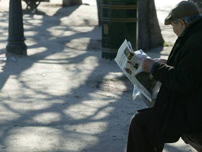 Un jubilado lee el peri&oacute;dico sentado en un banco de un parque.