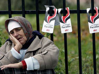 Una mujer, sentada en una calle de Pristina, con carteles electorales colgados detrás.