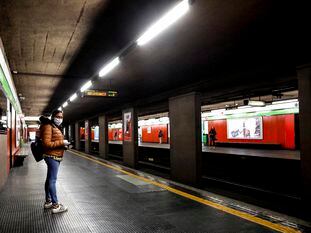 Una mujer protegida con una máscara espera en un solitario andén de una estación de metro, en Milán.