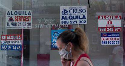 Una mujer con mascarilla pasa ante un comercio cerrado con varios carteles que anuncian su alquiler.
