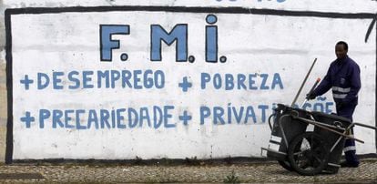 Un barrendero trabaja junto a una pintada crítica con el Fondo Monetario Internacional cerca de Lisboa.