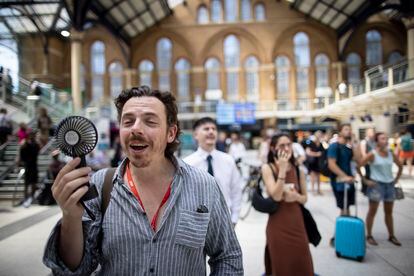 A man uses a fan to cool off on the London Underground.