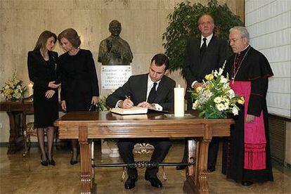 El príncipe de Asturias firma en el libro de condolencias ante sus padres, su esposa y un eclesiástico.