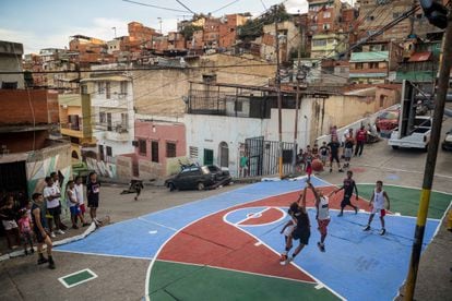 Niños y jóvenes juegan al baloncesto en una cancha restaurada por los vecinos en un barrio de Caracas.