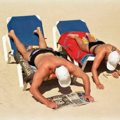 Una pareja lee en una postura incómoda mientras toma el sol en una playa de Mallorca.