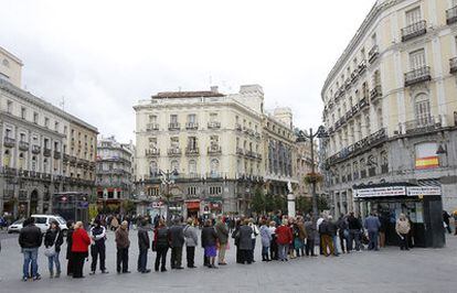 Un grupo de personas hacen cola en la madrileña Puerta del Sol para compra lotería de Navidad.