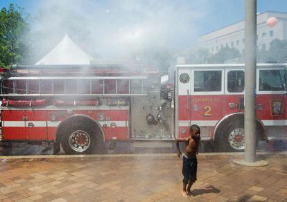 Un muchacho se enfría con una manguera de agua de un camión de bomberos en Washington, Estados Unidos.