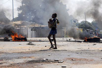 Una joven con una niña en brazos cruza una calle de Maputo afectada por los disturbios en Mozambique por la carestía de alimentos.