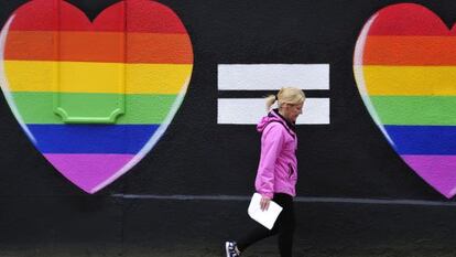 Una mujer camina junto a una pintada de dos corazones con los colores del arcoíris en Dublín.