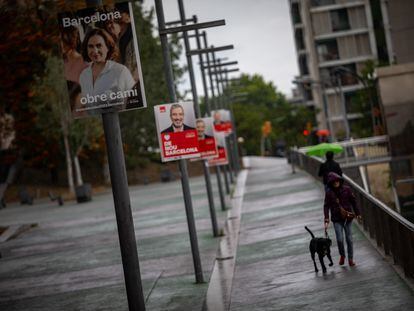 Varias personas pasean junto a carteles electorales por el barrio de Trinitat Nova de Barcelona.