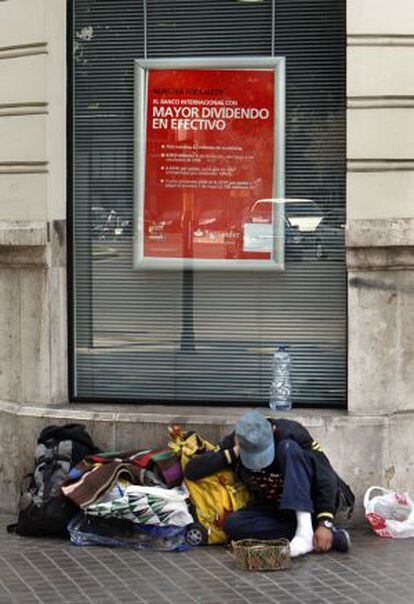 Una persona sin recursos sentada en la calle bajo un cartel de reparto de dividendos bancarios.