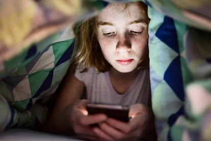 Girl lying under blanket in bed looking at her smartphone