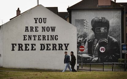 Dos personas caminan frente a un cartel en una fachada donde se puede leer "Estás entrando en la Derry libre" en el año 2010.