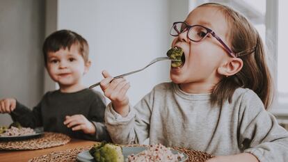 Siblings eat a healthy vegan lunch of broccoli and brown rice at home.
