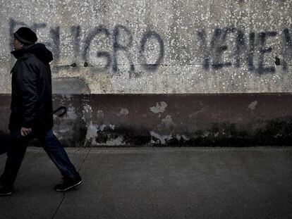 Un vecino cruza ante una pintada de advertencia sobre el lindano en las viviendas sociales de Torneiros, barrio de O Porri&ntilde;o.
