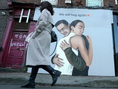 Una mujer pasa frente a un poster que dice "nos volveremos a abrazar" en Dublín, Irlanda.