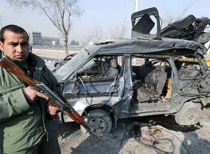 Un miembro de las fuerzas de seguridad afganas custodia uno de los vehículos dañados por el atantado suicida que tuvo lugar en la carretera al aeropuerto de Kabul.