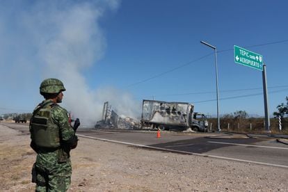 Un soldado hace guardia ante los restos de un vehículo quemado en la carretera, en Mazatlán (Sinaloa), este jueves.