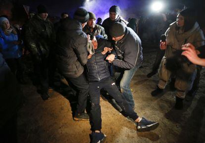 Tres manifestantes ayudan a un tercero a levantarse del suelo durante los enfrentamientos con la policía en la protesta contra los evacuados de Wuhan, en la localidad ucrania de Novye Sanzhari.