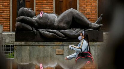 Una mujer pasa frente a una estatua con un lazo rosa, el símbolo del cáncer de mama.