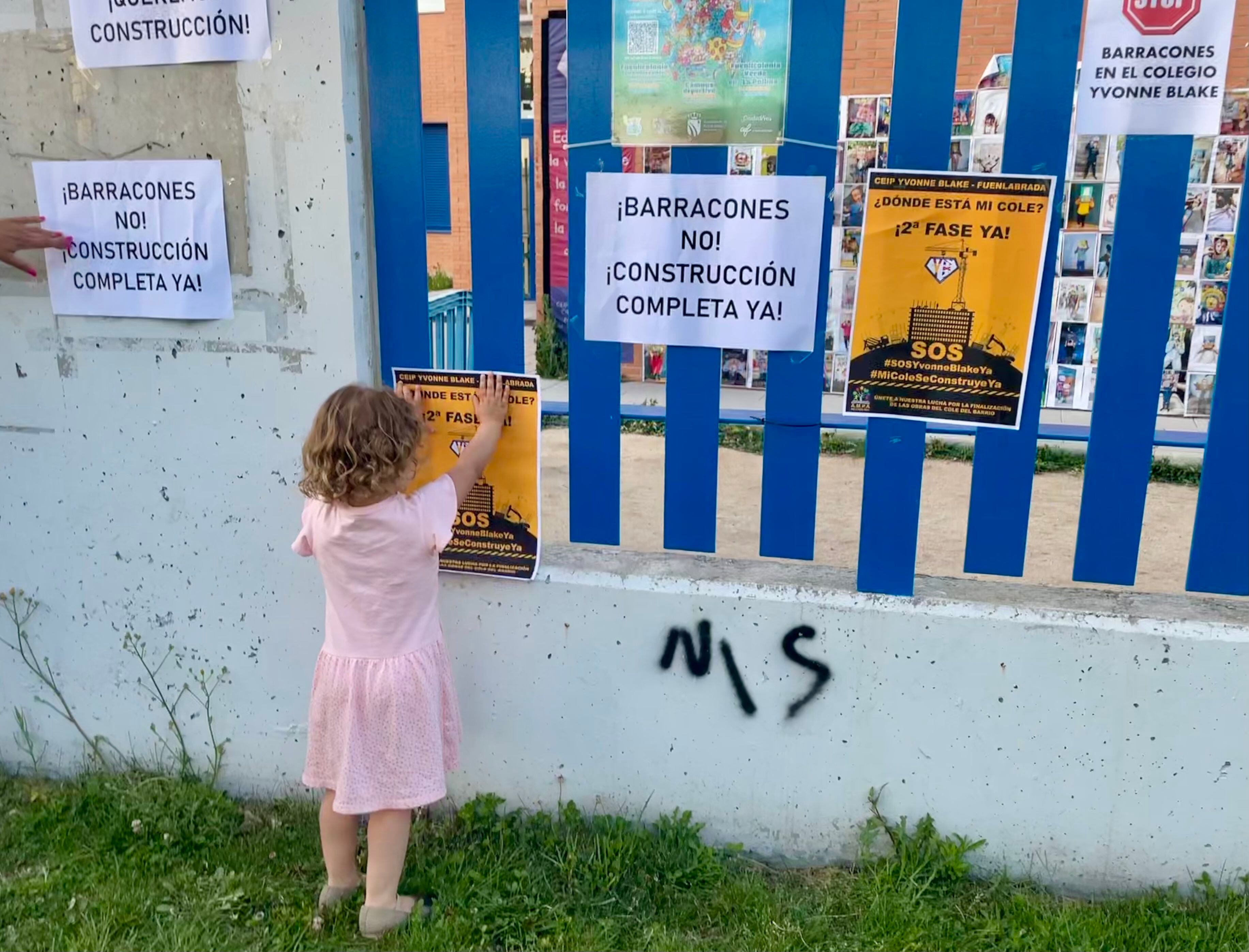 Un niña pega un cartel de protesta en la verja del colegio público Yvonne Blake, en Fuenlabrada, el viernes 5 de mayo. 