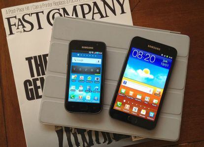 Samsung Galaxy Note, a la derecha, junto a un teléfono Samsun Galaxy, sobre un iPad y una revista