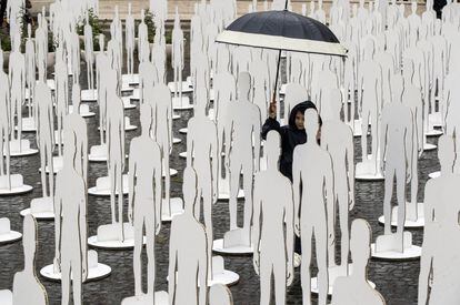Un niño camina bajo un paraguas entre algunas de las 1029 siluetas blancas instaladas para el evento "Trabajar para ganarse la vida" con motivo del Día Internacional del Trabajo, o Primero de Mayo, en memoria de las víctimas en el trabajo, en Roma.