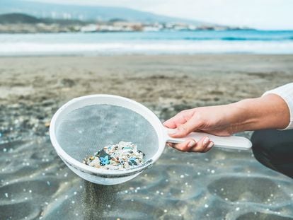 Una mujer limpiando microplásticos de la arena en la playa.