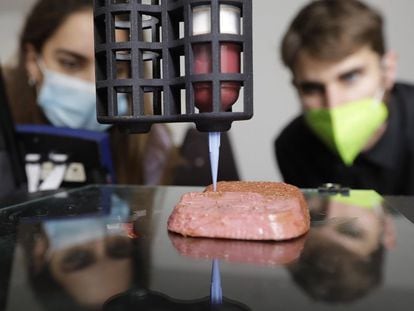 Dos personas observan como una impresora 3D de la empresa Novameat fabrica un filete de carne artificial.