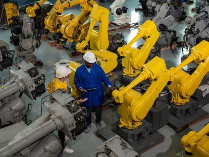 Dos operarios supervisa el proceso de fabricación y desarrollo de brazos robóticos de automatización personalizada, en un centro de distribución de robots industriales.
