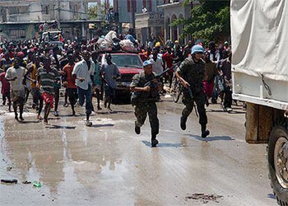 Un grupo de haitianos corre tras un camión con ayuda humanitaria mientras dos <i>cascos azules</i> tratan de protegerlo.