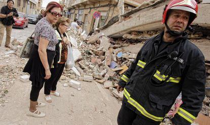 Un bombero y varios vecinos ante las ruinas de un edificio de Lorca.