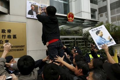 Un activista coloca un cartel ante la oficina de representación china en Hong-Kong con los rostros de los editores desaparecidos Lee Bo y Lu Bo.