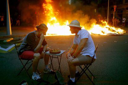 Dos hombres bromean jugando al ajedrez ante una de las barricadas en llamas en las calles de Barcelona en la noche de este viernes.