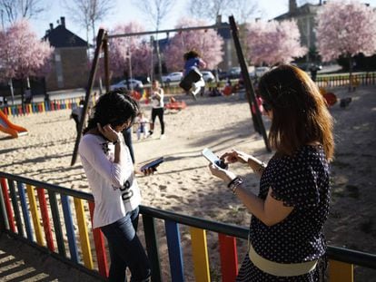 Dos mujeres usan su tel&eacute;fono m&oacute;vil al lado de un parque infantil
