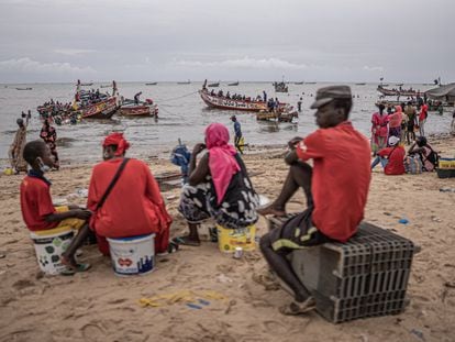 Un grupo de mujeres y jóvenes espera la llegada de los cayucos al puerto de Mbour, en Senegal, tras la jornada de pesca. Mbour es una localidad de tradición pesquera y en la que muchos migrantes han partido a lo largo de la historia en dirección a las islas Canarias.