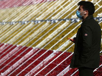 Un hombre con mascarilla ante la bandera gigante de LED en el puente de Juan Bravo en La Castellana de Madrid.