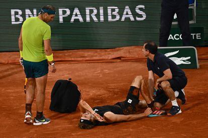 Alexander Zverev llora en el suelo tras la torcedura de tobillo ante la atenta mirada de Rafa Nadal.