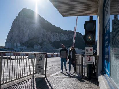 Dos personas atraviesan la verja de Gibraltar, con el Peñón de fondo.