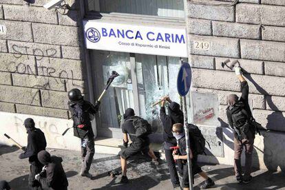 Varias personas golpean las cristaleras de un banco en el centro de Roma. Un grupo de unos 40 indignados ha prendido fuego a varios coches y asaltado tiendas y bancos.