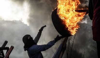 Un manifestante lanza un neumático ardiendo para montar una barricada en la plaza de la Independencia de Kiev.