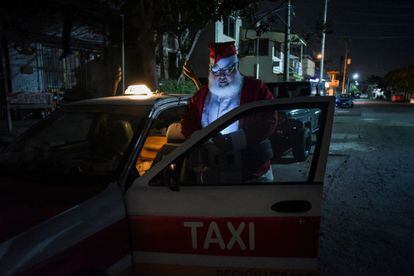 Un taxista vestido de Papá Noel mira su teléfono móvil junto a su taxi, en Boca del Río (México). El Gobierno mexicano reportó 12.485 nuevos casos y 861 muertes por la covid-19 en la última jornada hasta totalizar 1.362.654 contagios y 121.172 fallecidos.