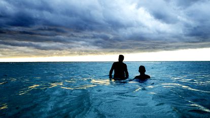 Dos hombres anónimos se bañan en una playa de Cuba bajo nubes de tormenta.