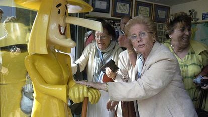 Una mujer toca las manos del muñeco que da nombre a la administración de lotería de Sort, La Bruixa d'Or (Lleida).