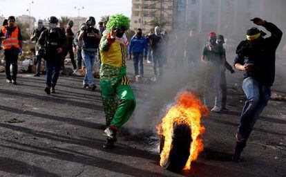 Un manifestante palestino disfrazado de payaso patea un neumático incendiado durante los enfrentamientos en Ramala, Cisjordania.