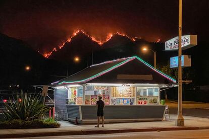 Un hombre en un restaurante mientras al fondo se ven las llamas que devoraban el jueves por la noche las colinas del Parque Nacional de Los Ángeles.