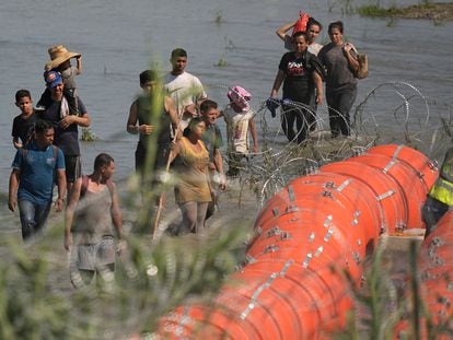Un grupo de migrantes intenta cruzar el río Bravo mientras trabajadores instalan la barrera acuática entre Eagle Pass y Piedras Negras, el pasado 11 de julio.