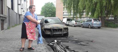 Una vecina de Molenbeek junto a uno de los coches quemados.