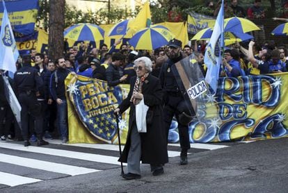 Una mujer camina ante los aficionados de Boca concentrados fuera del hotel de su equipo en Madrid.
