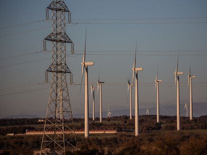 Molinos de un parque eólico junto a una torre del tendido eléctrico en Cataluña.